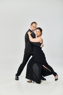 Gri arka planda izole edilmiş, tango dansı yapan olgun ve çekici bir çiftin yan görüntüsü.