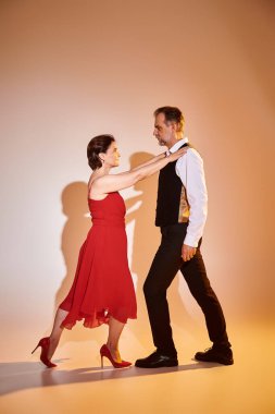Portrait of mature attractive couple in red dress and suit dancing on grey background clipart