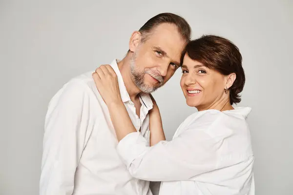 stock image Portrait of middle aged smiling couple hugging and looking at camera on grey background