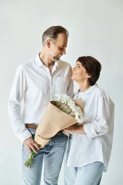 白いシャツの中年男性は 灰色の背景に魅力的な女性に花を贈ります — ストック写真