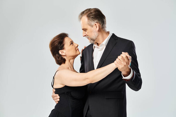 Снимок зрелой привлекательной пары в танцевальной позе танго, изолированной на сером фоне