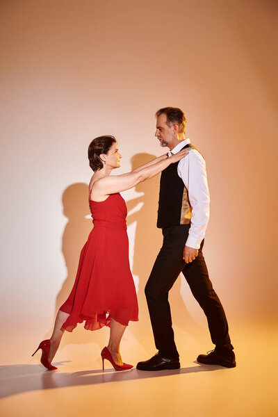 Портрет зрелой привлекательной пары в красном платье и костюме, танцующей на сером фоне