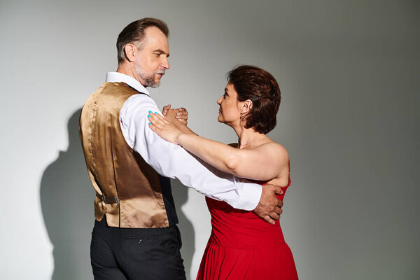 Портрет зрелой привлекательной пары в красном платье и костюме, танцующей на сером фоне