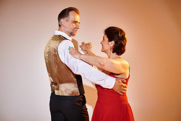 Пара средних лет в красном платье и костюме танцуют танго с желтым светом на сером