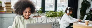 A woman of diverse descent sits in deep thought in front of a laptop computer, immersed in work or study, in a modern coworking space. clipart