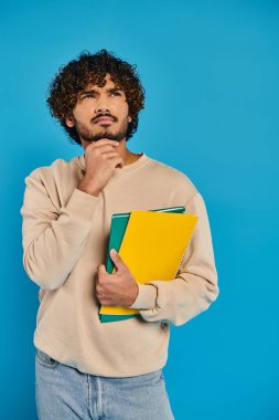 Kıvırcık saçlı Hintli bir öğrenci, bir stüdyo ortamında istihbarat ve gayret saçan bir klasör tutuyor..