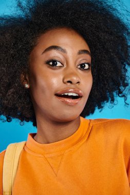 Şehvetli bir afro saçı olan Afrikalı bir üniversite öğrencisi stüdyoda mavi bir arkaplanda güven içinde poz veriyor..