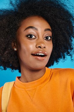 An African American college student with a voluminous afro posing confidently against a blue backdrop in a studio. clipart
