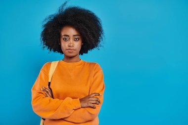 Şehvetli afro saçlı şık bir Afro-Amerikan kadını canlı, mavi bir arka planın önünde duruyor..