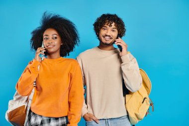 An interracial man and woman stand next to each other in a studio, talking on smartphones, showcasing diversity and unity. clipart