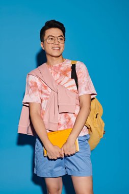 Şık bir genç adam, mavi bir arka plana karşı enerjik bir şekilde şık bir şekilde poz verir..