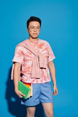 Şık bir genç adam canlı bir mavi duvarın önünde poz verir, kendine güveni ve karizması vardır..