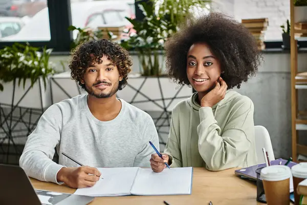 stock image A man and a woman of diverse backgrounds working together on a laptop at a modern coworking space.