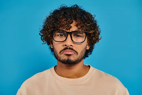 カーリーヘアとメガネを持つインドの学生は スタジオの設定で青い背景に自信を持ってポーズします — ストック写真