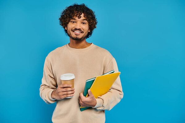 A man, dressed casually, holding a book and a cup of coffee.
