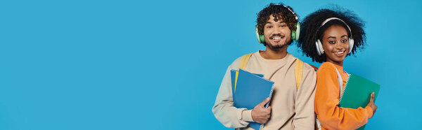 Межрасовая пара студентов стоят бок о бок в повседневной одежде, демонстрируя единство и разнообразие на голубом фоне..