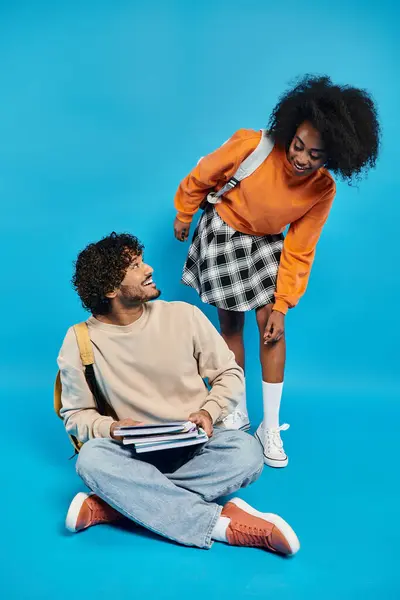 stock image A pair of interracial students sit side by side on the ground, engaged in conversation and contemplation.