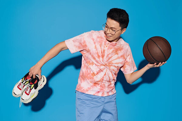 A stylish young man confidently holds a basketball and shoes, exuding enthusiasm and readiness for sports.