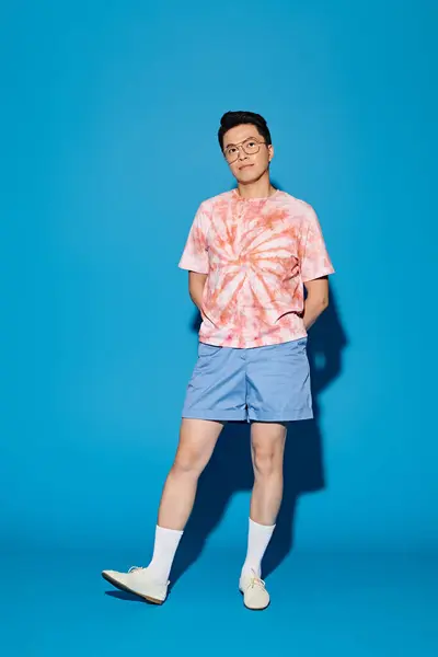 stock image A stylish, good-looking young man in trendy attire posing actively in front of a vibrant blue backdrop.