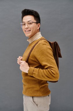 A stylish young man in glasses and a brown sweater poses elegantly. clipart