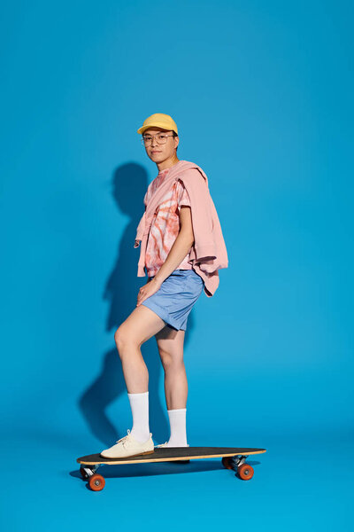 A trendy, good-looking young man energetically poses on a skateboard against a vibrant blue background.