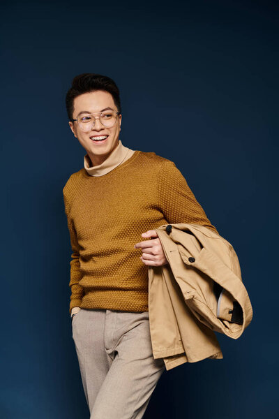 A fashionable young man exudes elegance in a brown sweater and tan pants, confidently posing for the camera.