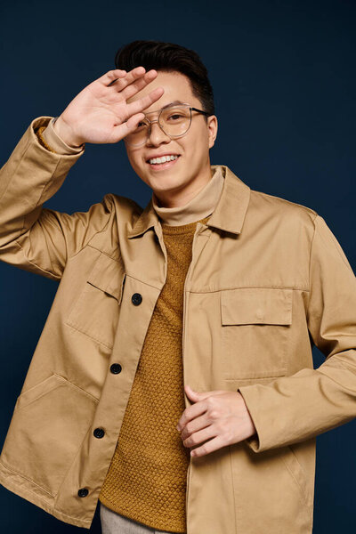 A fashionable young man with glasses poses confidently in a tan jacket, exuding elegance and sophistication.