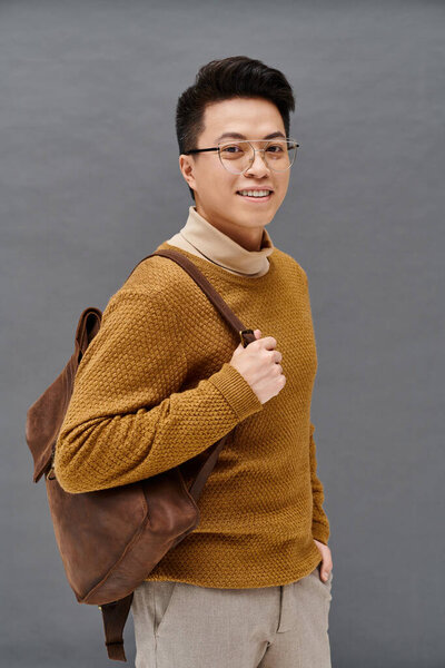 A fashionable young man with glasses and a brown backpack poses confidently in elegant attire.