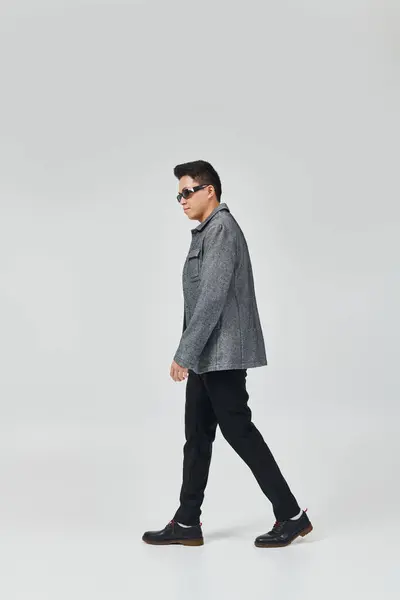 一个穿着灰色夹克和黑色裤子的时髦年轻人自信地漫步 — 图库照片