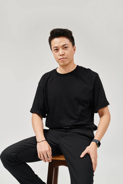 Модный молодой человек в элегантной одежде, изящно сидящий на деревянном стуле.