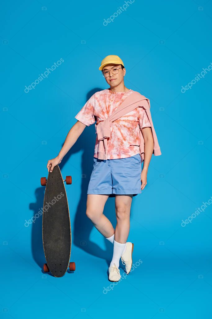 A stylish man in trendy attire energetically holds a skateboard in front of a vibrant blue backdrop.
