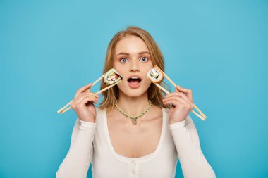 A beautiful woman with blonde hair holding two chopsticks over her eyes in a playful and artistic pose. clipart