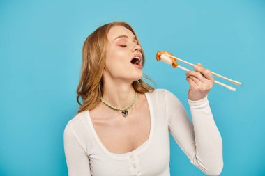 A blonde woman elegantly holds chopsticks, ready to savor delicious Asian cuisine. clipart