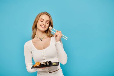 A chic blonde woman holds a tray of sushi and chopsticks, ready to indulge in a delightful Asian culinary experience. clipart