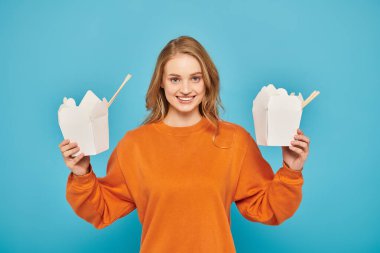 A woman with blonde hair holding two boxes of Asian food in her hands, looking pensive and contemplative. clipart