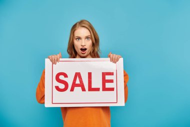 A woman hides herself behind a sale sign on bright blue backdrop clipart