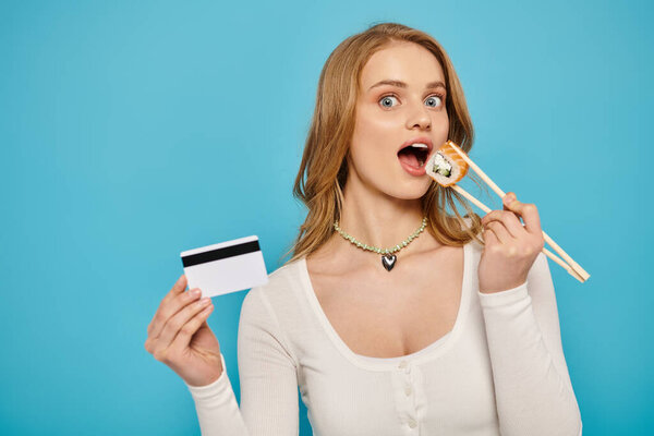 Blonde woman confidently holds chopsticks and a credit card, ready to indulge in Asian cuisine.
