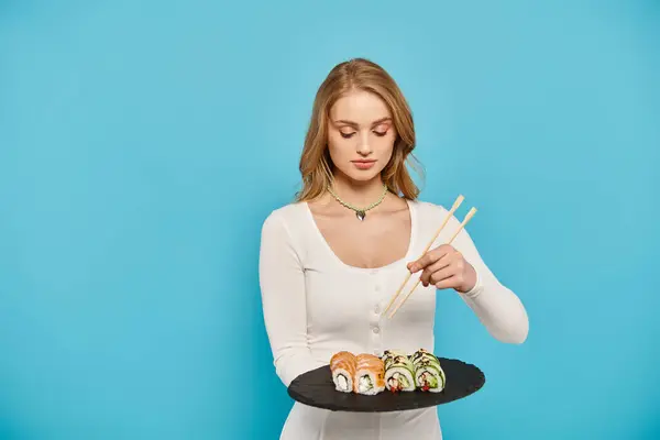一位漂亮的金发女子小心翼翼地拿着一盘寿司和筷子 展示着品尝亚洲美食的艺术 — 图库照片