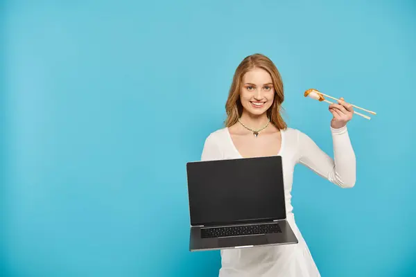 一个金发碧眼的女人拿着笔记本电脑 手里拿着亚洲菜 展示着科技和烹调的混合乐趣 — 图库照片