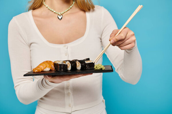 Cropped view of stylish woman holds a plate of sushi and chopsticks, ready to indulge in the delicious Asian delicacy.