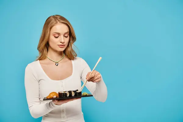 Blondynka Wdziękiem Trzyma Talerz Sushi Pałeczkami Pokazując Piękno Kuchni Azjatyckiej — Zdjęcie stockowe