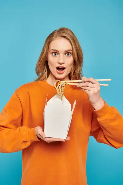シックなブロンドの女性はエレガントに箸と麺の箱を保持し アジア料理への感謝を示しています — ストック写真