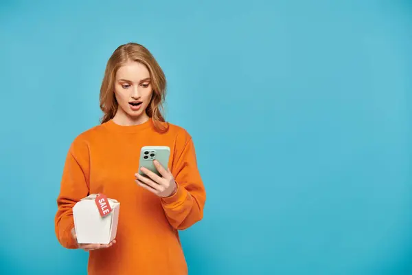 オレンジ色のセーターのスタイリッシュな女性は自信を持って携帯電話を保持し その上に食べ物のセールスタグ — ストック写真