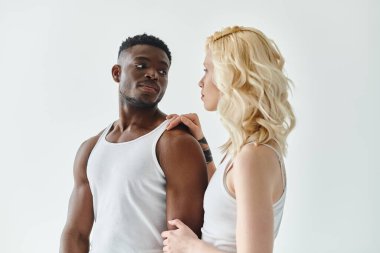 Genç, çok kültürlü bir çift gri bir arka plana karşı stüdyoda bir arada duruyor, birlik ve beraberlik sergiliyorlar..