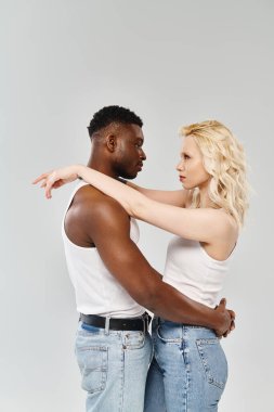 A young multicultural couple standing together on a grey background, embodying unity and connection through their presence. clipart