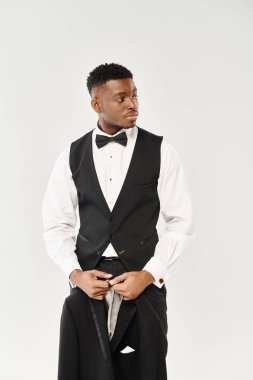 Handsome African American groom standing in a stylish tuxedo and bow tie against a grey background. clipart
