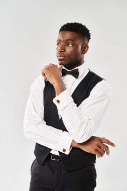 Smokinli genç, yakışıklı bir Afrikalı Amerikalı damat gri bir arka planla stüdyo ortamında kendine güvenen bir poz veriyor..