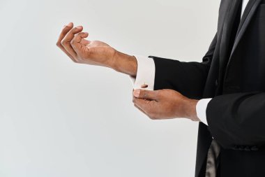 A young and handsome African American groom in a suit extending his hand for a handshake in a studio against a grey background. clipart