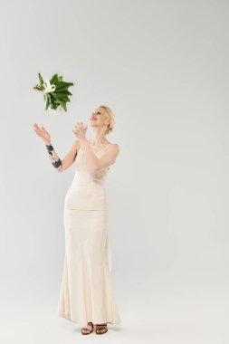 Güzel bir sarışın gelin beyaz bir elbise içinde zarif bir şekilde duruyor, zarif bir şekilde buketi yakalıyor, zarafet ve güzellik saçıyor..