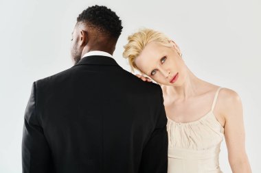 Gelinlik giymiş güzel bir sarışın gelin ve bir Afrikalı Amerikalı damat gri bir arka planda stüdyoda yan yana duruyorlar..